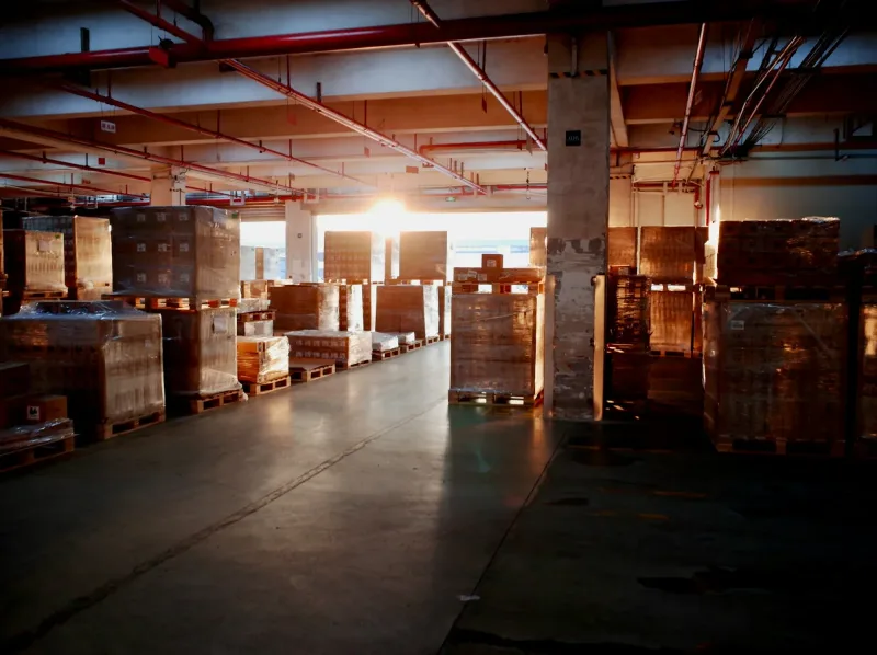 Allée d'un entrepôt de distribution en fin de journée, palettes filmées alignées de part et d'autre